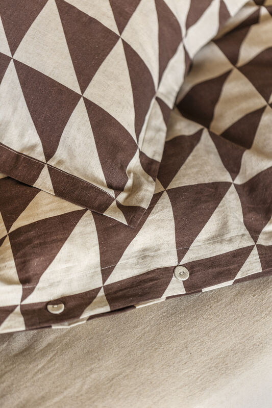 Närbild på mönstrade sängkläder i brunt och beige med ett harlekinmönster av trianglar.