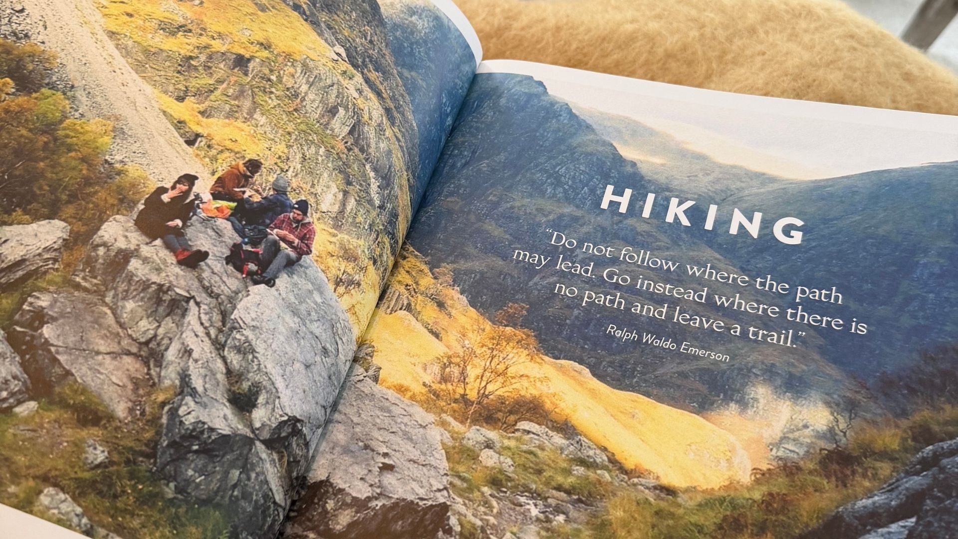 En tjock, uppslagen bok som ligger på ett rustikt träbord utomhus. Bakgrunden är mjukt fokuserad och visar lummig grönska och träd i dagsljus.