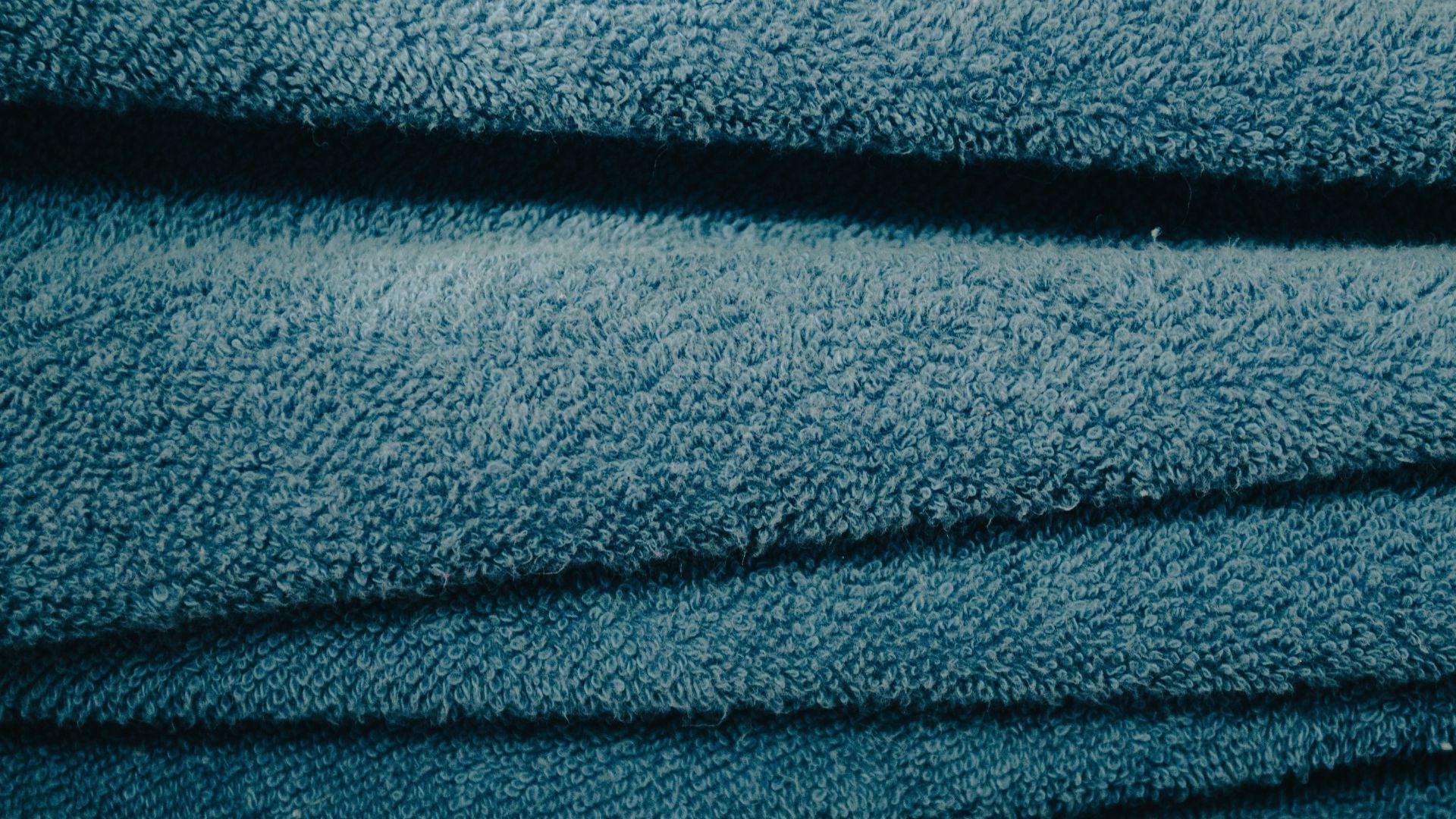 Närbild på texturen av en mjuk, mörkblå frottéhandduk med tydliga öglor och veckat tyg.