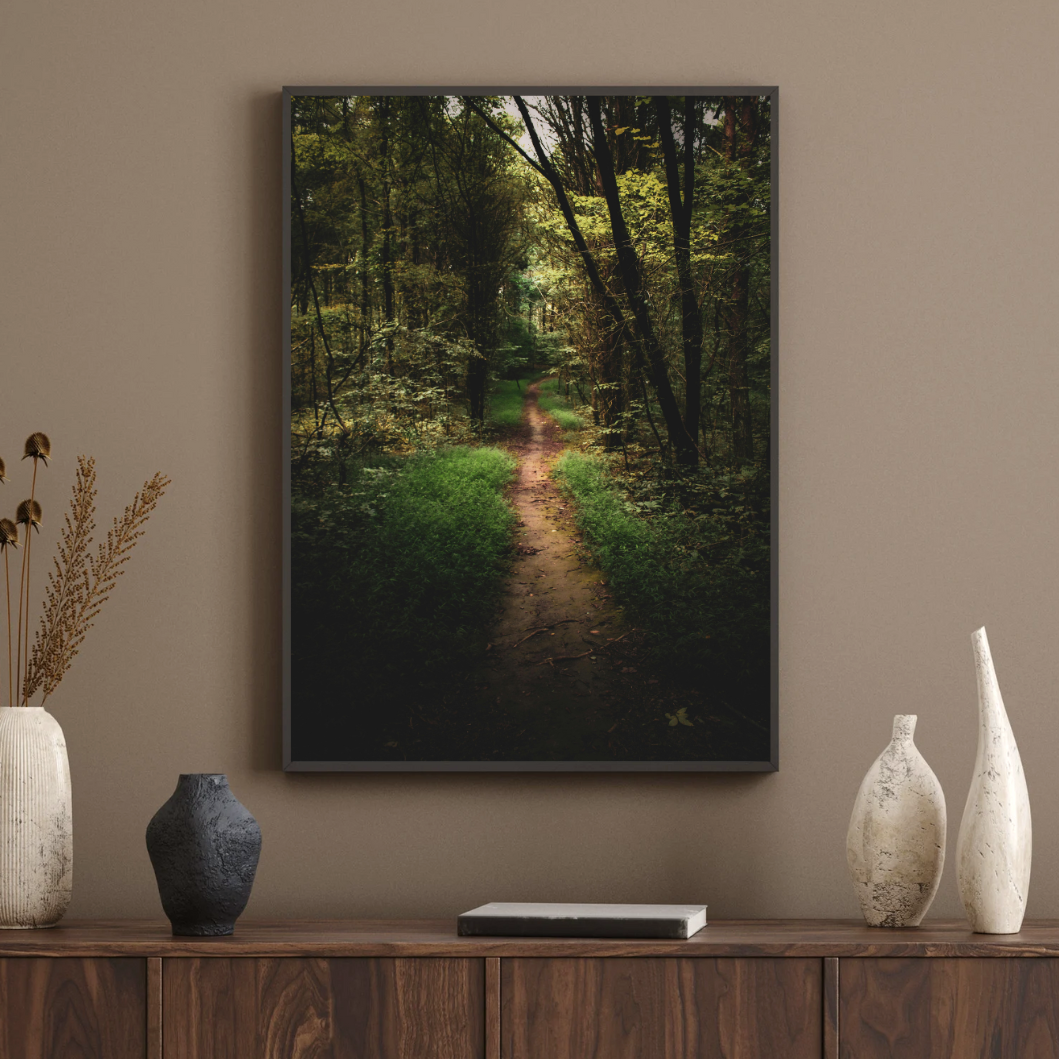 En inramad tavla med ett motiv av en lummig skogsstig som hänger ovanför en skänk med dekorativa vaser.