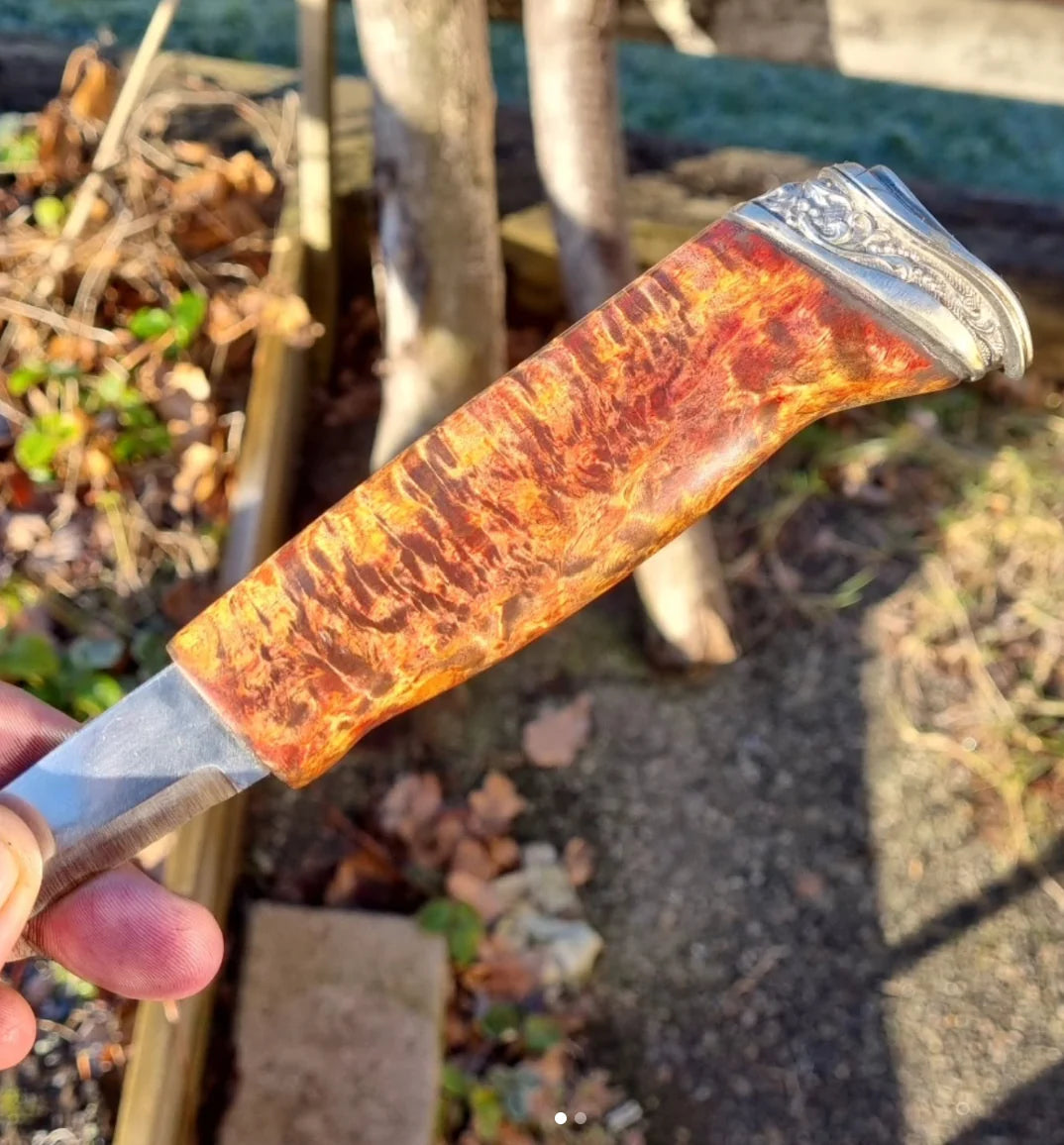 Handgjord kökskniv med mönstervällt damaskusstål och ett ergonomiskt skaft i djupröd, skimrande resin, vilande på en skärbräda i trä.