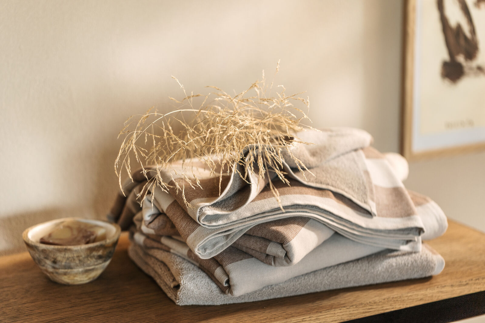 Randig handduk i bomull designad av Gustav Ovland, stylad med torkat gräs och en träskål på en träyta.