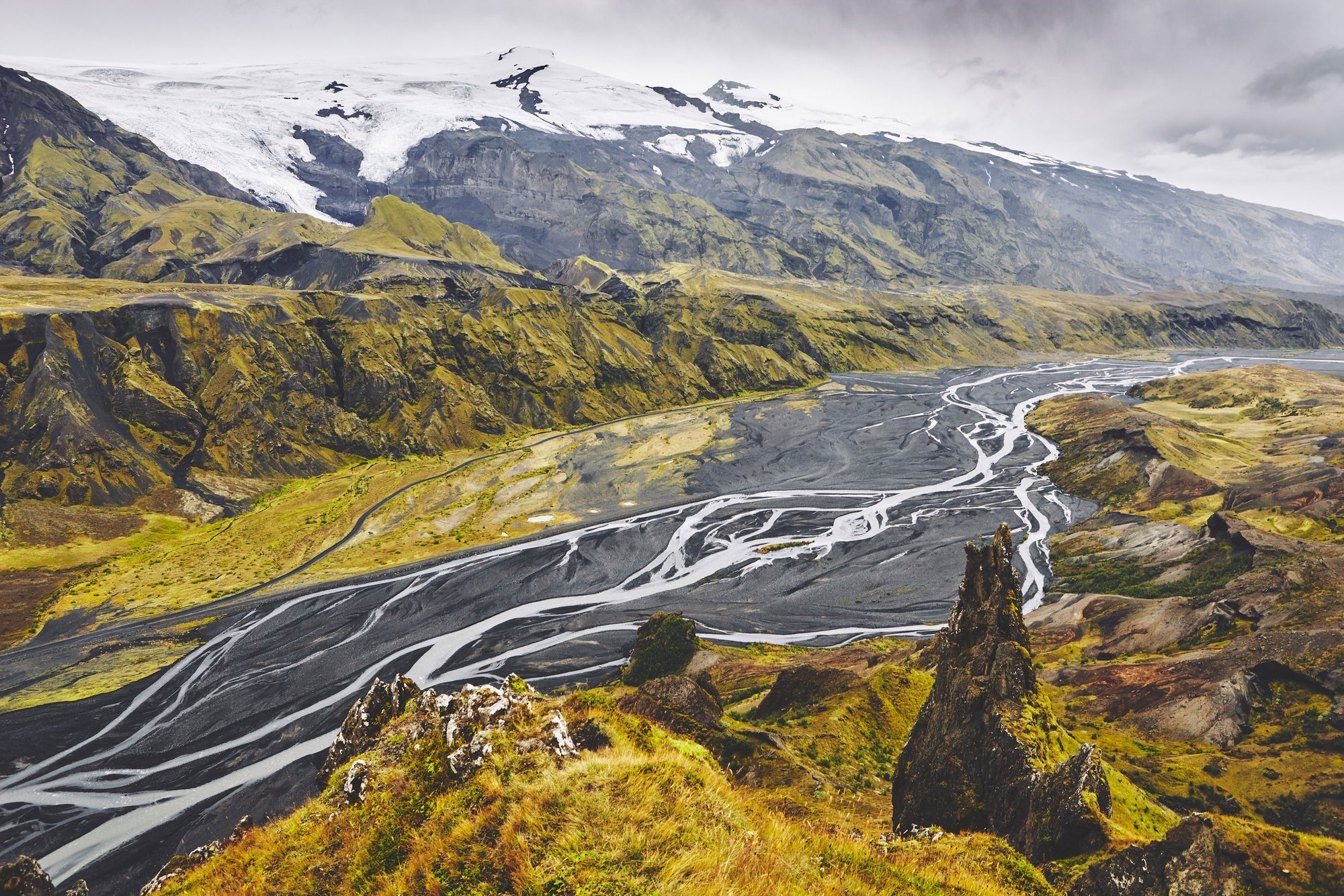 Ett kargt vulkanlandskap sett ovanifrån, där glaciärfloder delar upp sig i ett komplext, organiskt nätverk över mörk aska. En visuell analogi för hur outsider-idéer sprider sig: inte genom en huvudfåra, utan genom tusentals alternativa vägar som tillsammans formar ett nytt landskap.